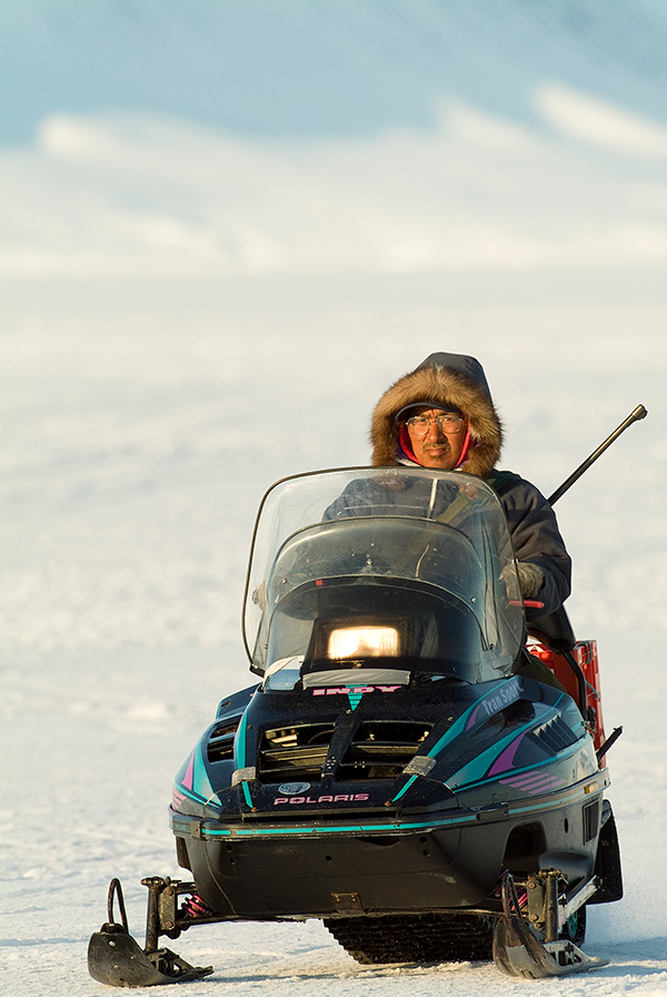 David Angnatsiak A warmly dressed man rides a snowmobile.