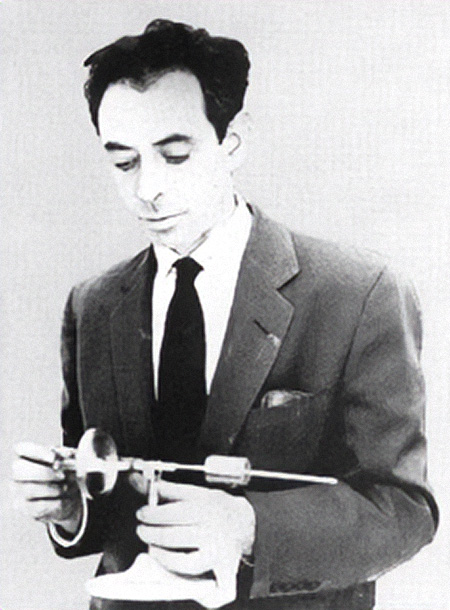 Postwar Frank Oppenheimer A black-and-white photo shows a young man in a suit and tie glances down at the instrument in his hand.