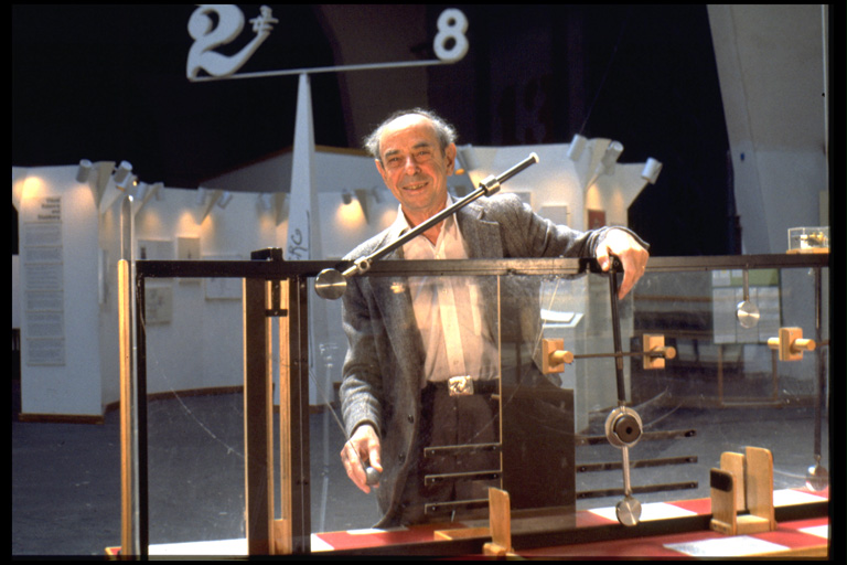 Pendulum exhibit Color photo shows an older man standing behind a contraption on a table.