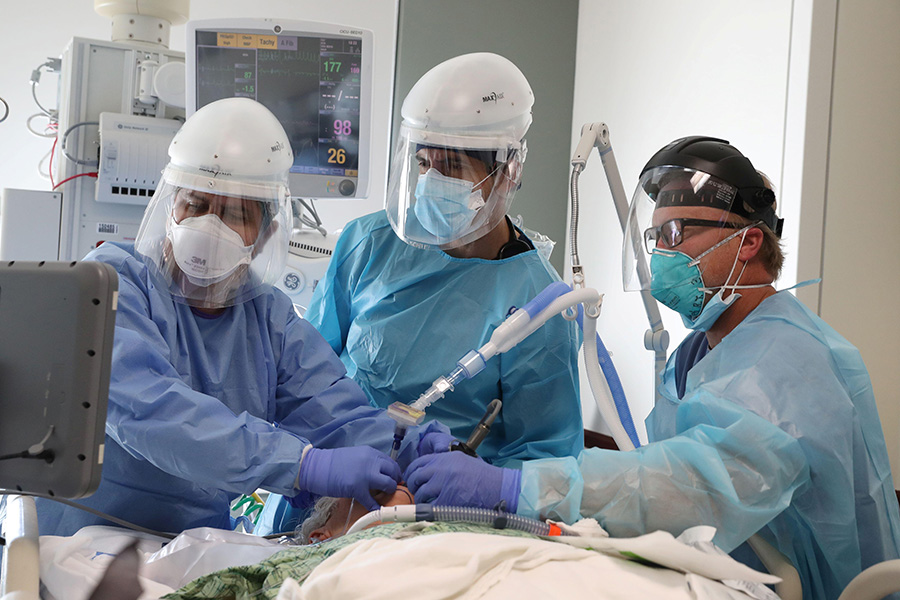 Covid has brought grief A photograph shows three healthcare workers dressed in masks, face shields, gowns and gloves around the bed of a patient in intensive care unit. They are intubating the patient and watching progress of the intubation on a screen.