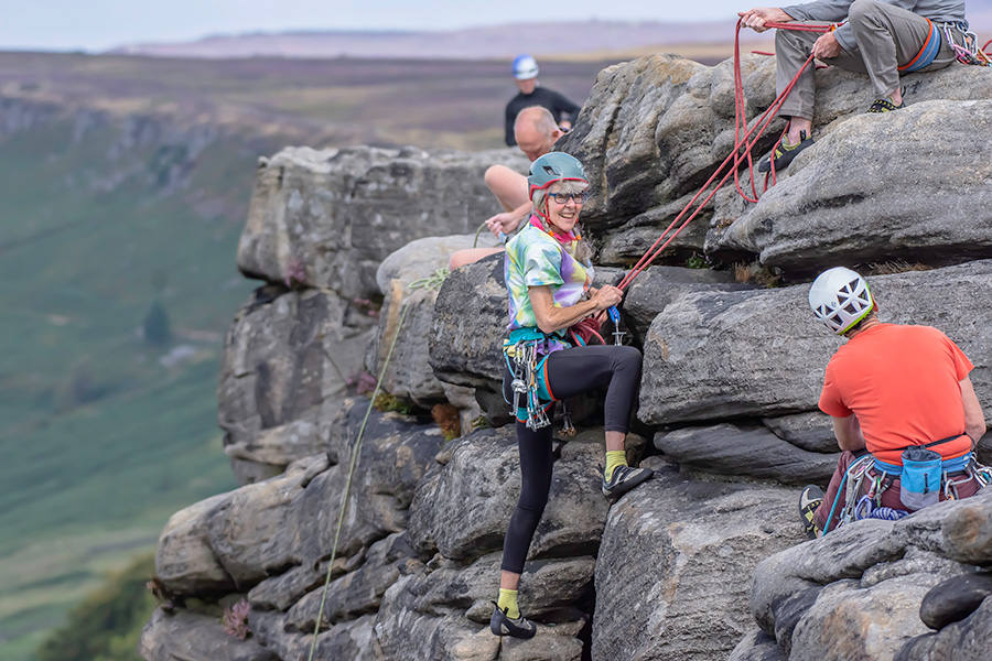 Rock-climbing A mature woman stands at the top of a cliff having completed a rock climb. She is smiling.