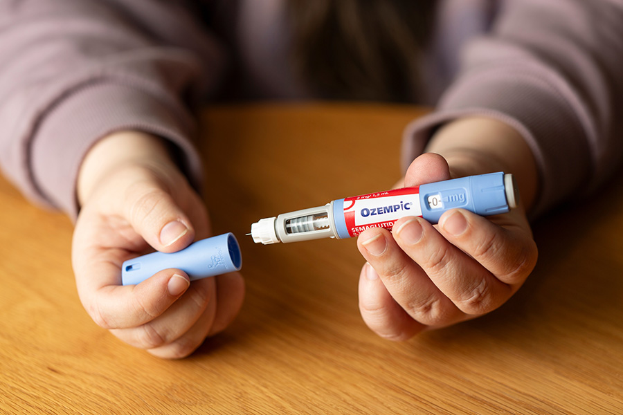 Ozempic A person holds a light blue Ozempic pen, with the cap in one hand, and the pen in the other, with a needle on its tip.