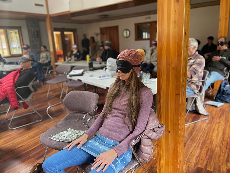 Facilitators in training Photo shows a woman wearing a sleeping mask, sitting in a chair in meeting room with others also wearing sleeping masks, all looking toward the front of the room.