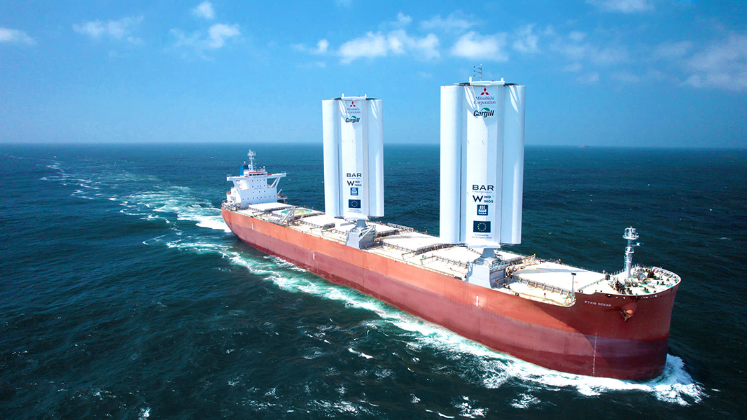 Pyxis Ocean Photograph of a ship in the water, with rust-red hull and two large structures — the sails — that look like several upright cylinders joined together.