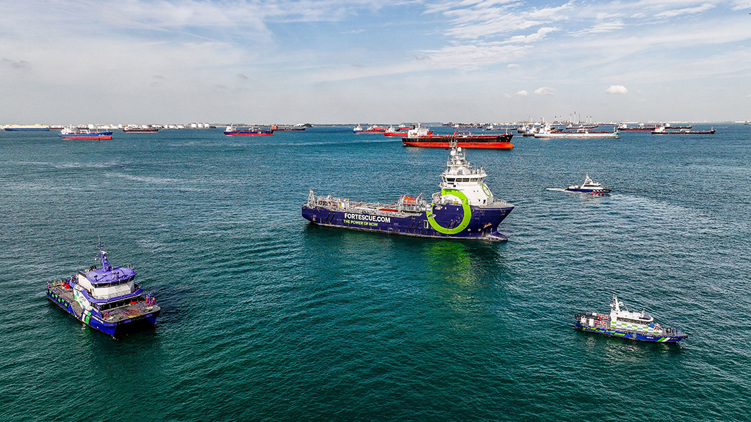 Ammonia-powered ship Photograph a variety of vessels moored in a seaport. Near the front is a ship that says “fortescue.com, the power of now” on its side.