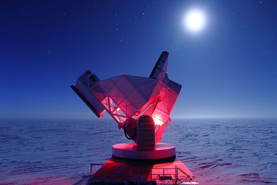 South Pole Telescope Photo shows part of the telescope lit in red on a moonlit night, with snow visible all the way to the horizon.