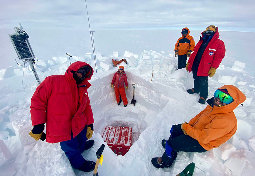 Cool work Several people in cold-weather clothing pose near a hole they’ve dug in a glacier, with various pieces of equipment nearby.