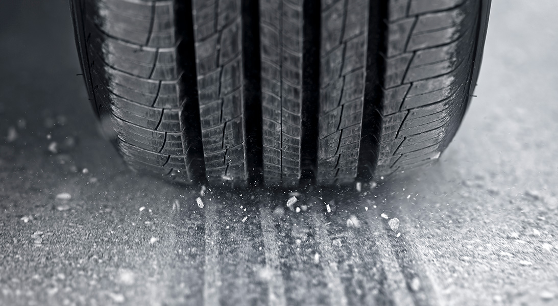 Car tire Close-up photograph of a car tire and an asphalt road surface covered with dust and grit.