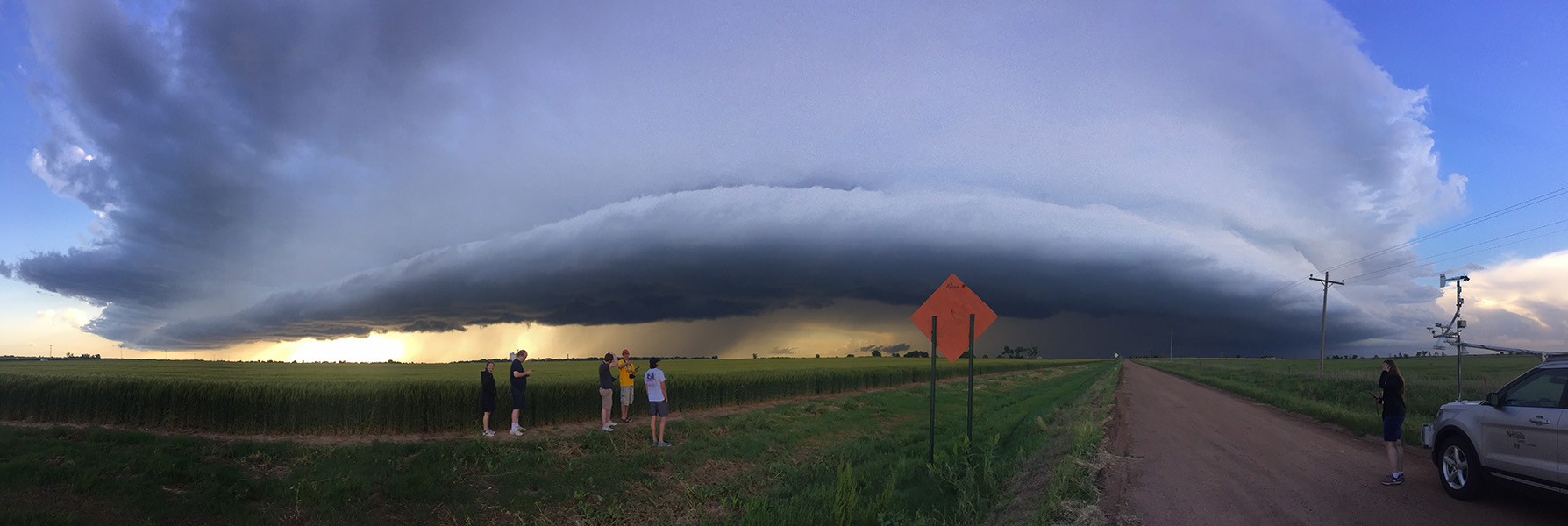 Storm chaser Five college students stand at a cornfield’s edge observing a giant low storm cloud.