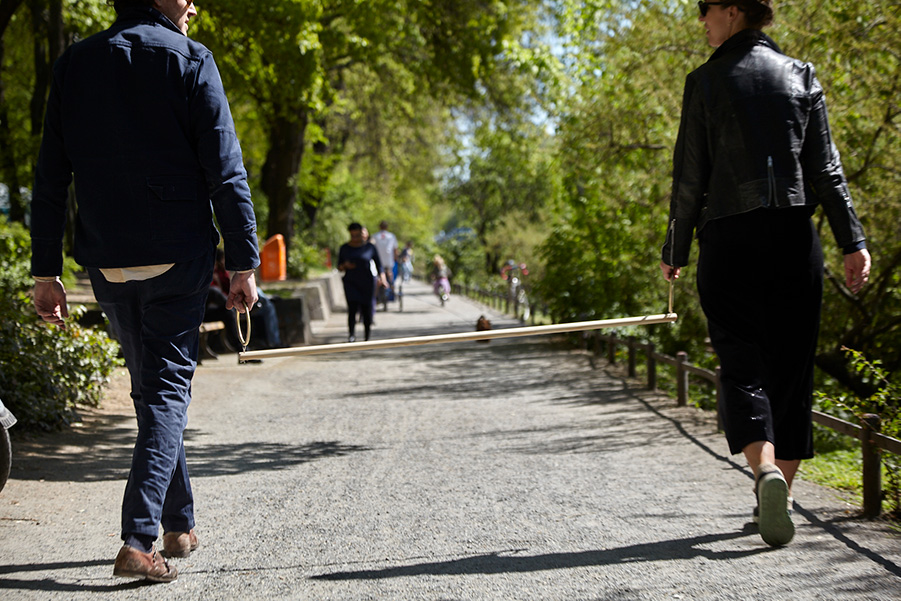 Walking Stick Photograph of two people walking, each one holding a brass ring attached to the ends of a long walking stick.