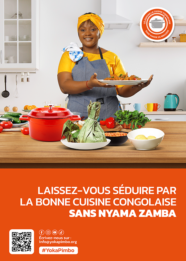 Yoka Pimbo A woman in grey apron and bright yellow headscarf and shirt is smiling behind a counter and holding up a plate of food. Various other vessels of food are displayed on the counter in front of her.